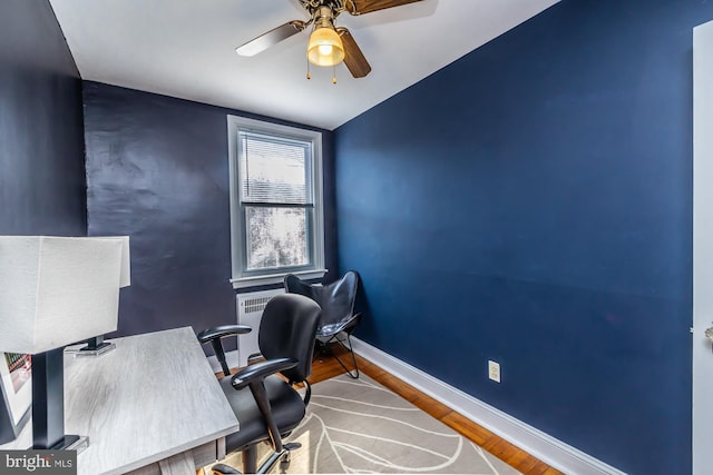 office featuring an accent wall, wood finished floors, a ceiling fan, and baseboards