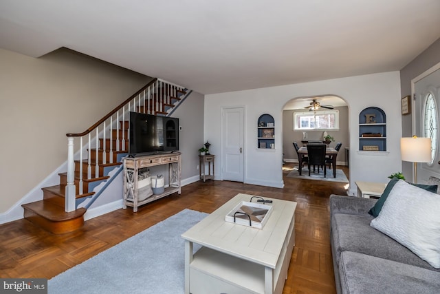 living room featuring arched walkways, a ceiling fan, stairs, and baseboards