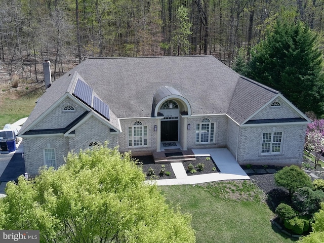 view of front of house with brick siding, a front yard, a view of trees, and a chimney