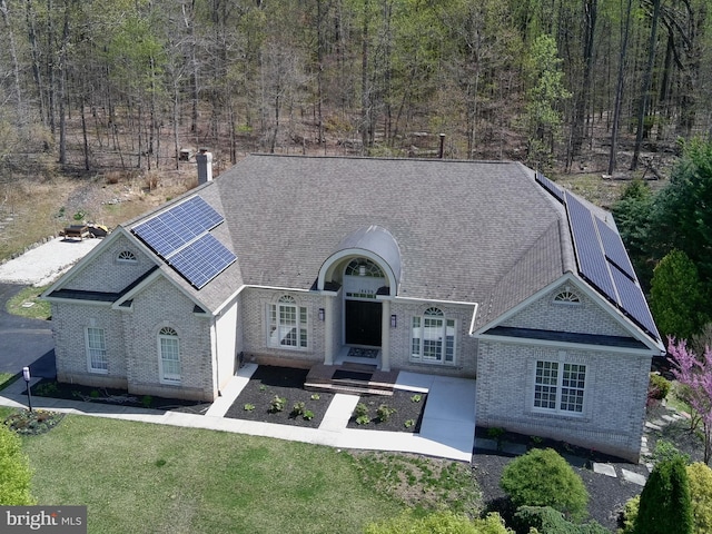 view of front of property with roof mounted solar panels, a shingled roof, a front yard, and brick siding
