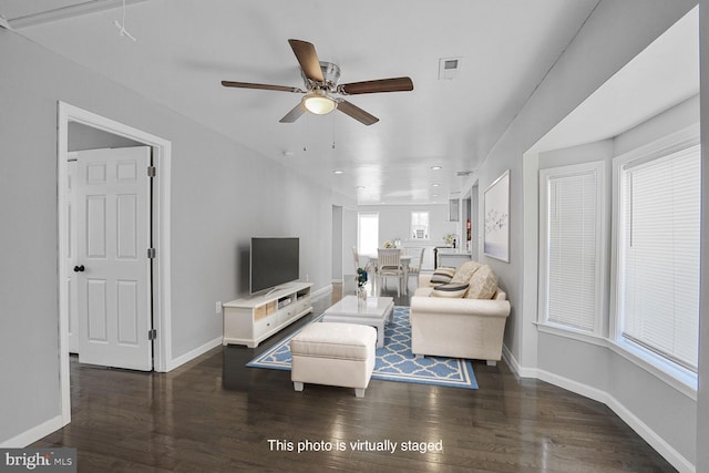 living area featuring ceiling fan, visible vents, baseboards, and dark wood-style floors