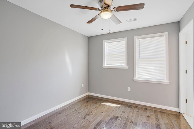 empty room with visible vents, a ceiling fan, baseboards, and wood finished floors