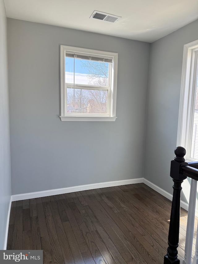 unfurnished room with dark wood-style floors, visible vents, and baseboards