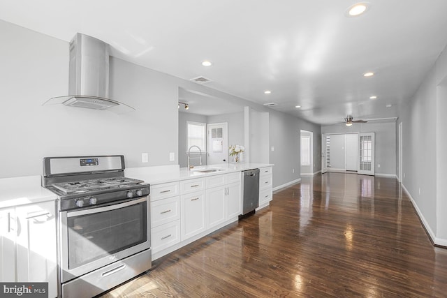 kitchen featuring a sink, wood finished floors, white cabinetry, stainless steel appliances, and wall chimney exhaust hood