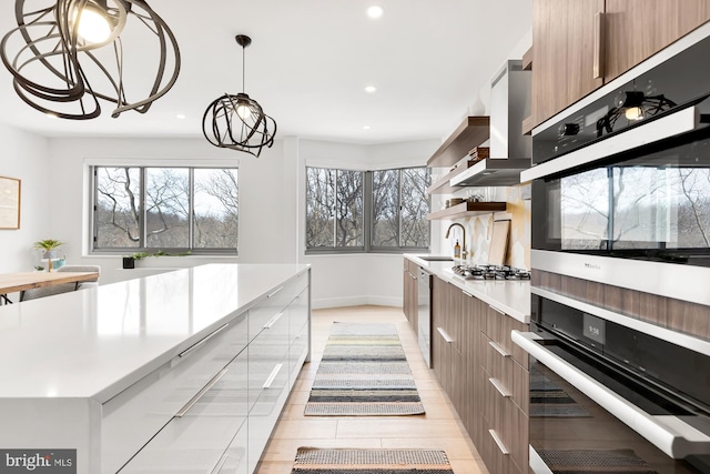 kitchen with modern cabinets, a sink, stainless steel appliances, wall chimney range hood, and light countertops