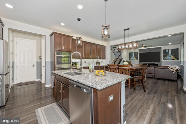 kitchen with light stone countertops, dark wood-style floors, a sink, appliances with stainless steel finishes, and open floor plan