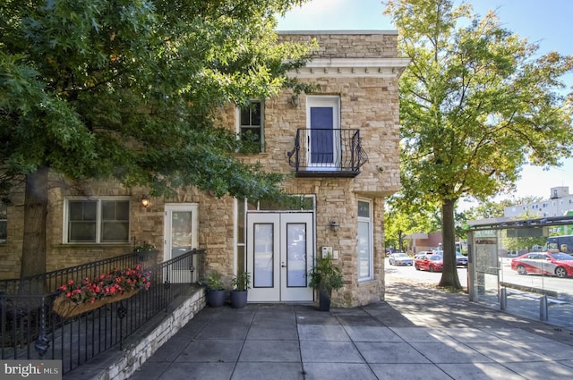 view of front facade featuring french doors, stone siding, and a balcony