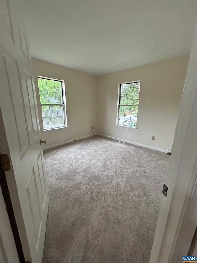 carpeted spare room featuring plenty of natural light, visible vents, and baseboards