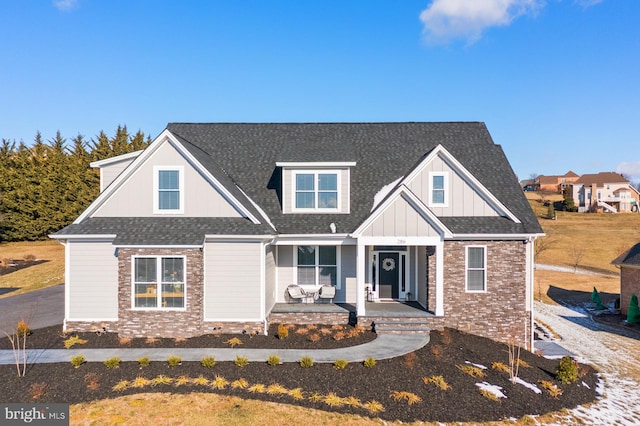 view of front of house featuring board and batten siding, brick siding, covered porch, and roof with shingles