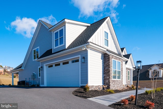 view of side of home with driveway, stone siding, board and batten siding, a shingled roof, and a garage