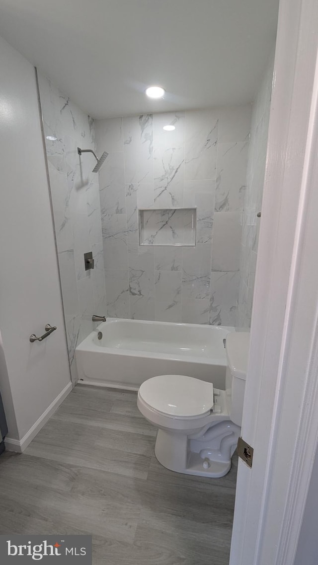 bathroom featuring toilet, wood finished floors, baseboards, and shower / bathtub combination