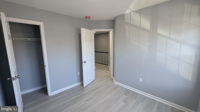 unfurnished bedroom with a closet, light wood-style flooring, and baseboards