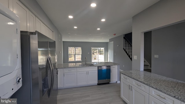 kitchen featuring stainless steel fridge with ice dispenser, stacked washer and dryer, dishwashing machine, white cabinetry, and a sink