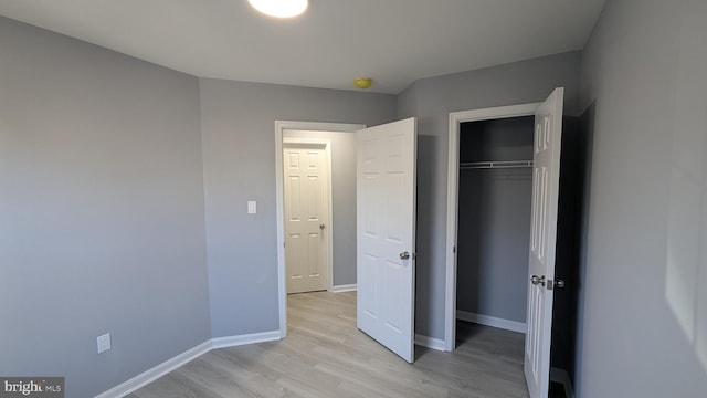 unfurnished bedroom with a closet, baseboards, and light wood finished floors