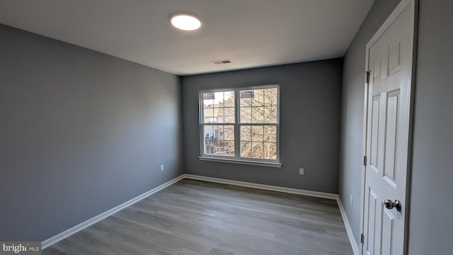 empty room featuring wood finished floors, baseboards, and visible vents