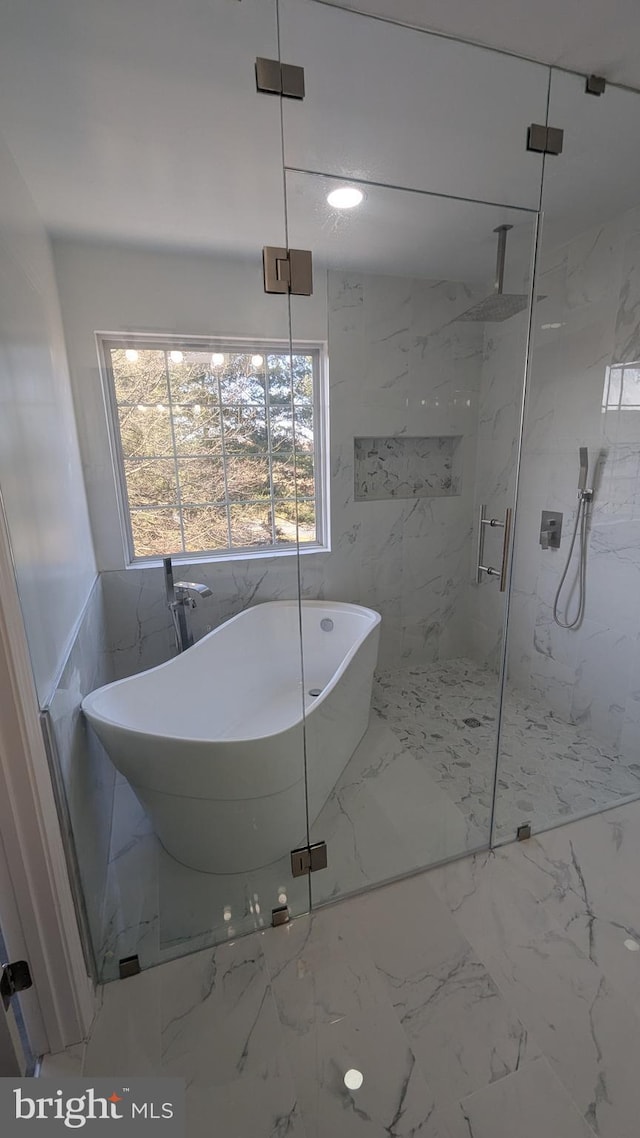 full bath with a freestanding tub, a marble finish shower, marble finish floor, and stone wall