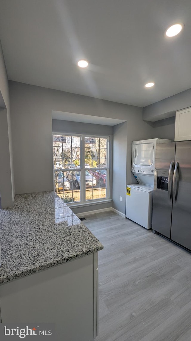 kitchen featuring light stone counters, light wood finished floors, stacked washing maching and dryer, white cabinetry, and stainless steel fridge