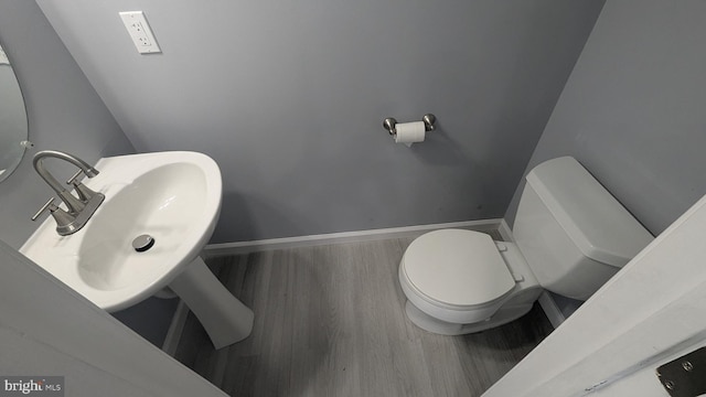 half bathroom with toilet, wood finished floors, baseboards, and a sink