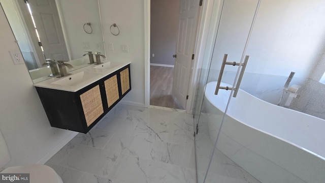 bathroom with double vanity, a freestanding tub, marble finish floor, and a sink