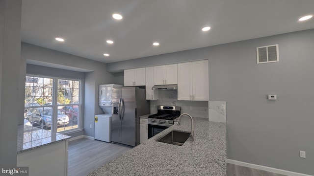 kitchen featuring visible vents, stacked washer and dryer, under cabinet range hood, a sink, and stainless steel appliances