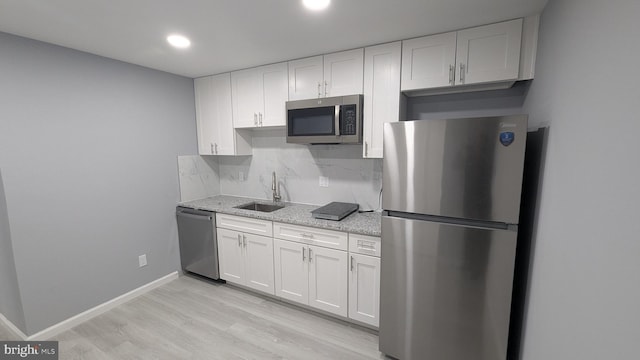 kitchen with backsplash, stainless steel appliances, light wood-style floors, white cabinetry, and a sink