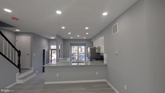 kitchen with visible vents, a peninsula, stainless steel appliances, light wood-style floors, and white cabinetry