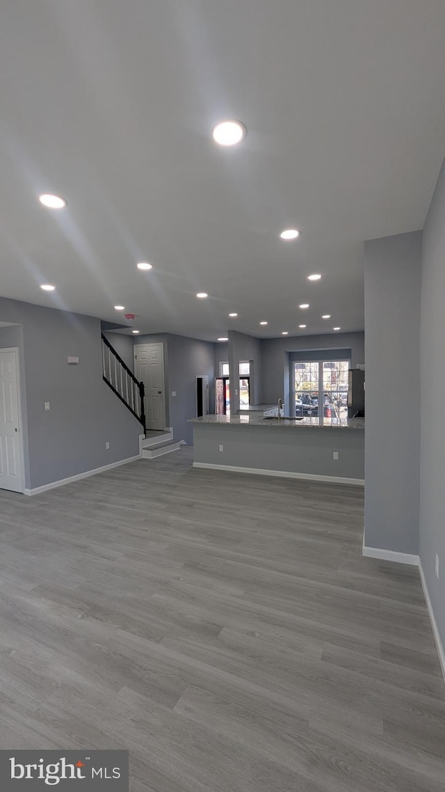 unfurnished living room featuring stairway, recessed lighting, baseboards, and wood finished floors