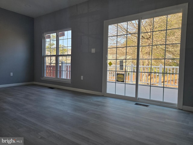 empty room with dark wood-style floors, visible vents, and baseboards