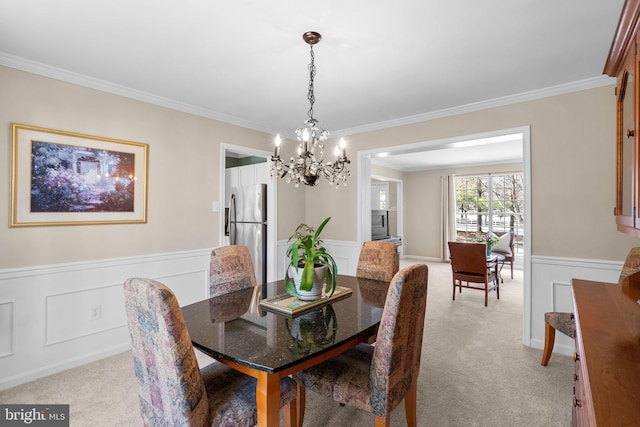 dining room with a wainscoted wall, light carpet, ornamental molding, and a decorative wall