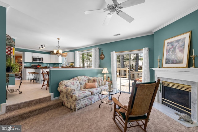 living area with visible vents, ceiling fan with notable chandelier, a high end fireplace, crown molding, and light colored carpet