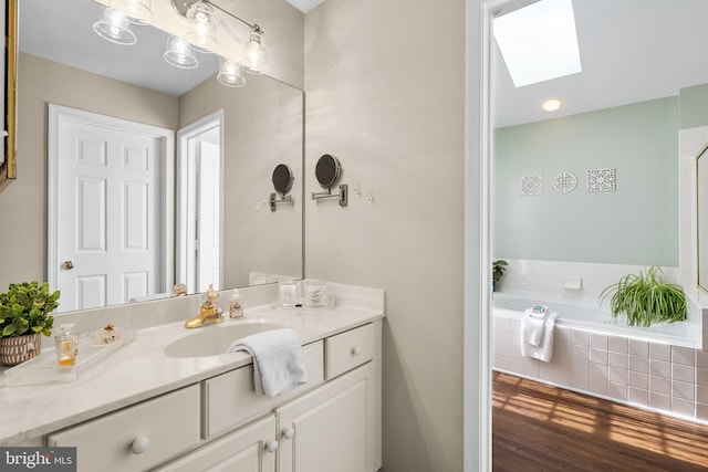 full bathroom with vanity, a relaxing tiled tub, a skylight, and wood finished floors