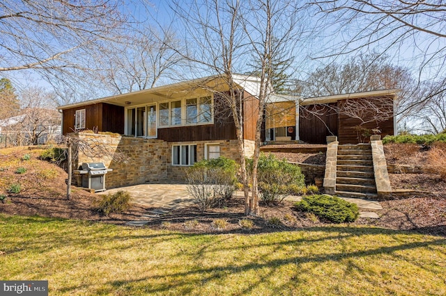 rear view of property featuring a patio, stairway, a yard, and stone siding