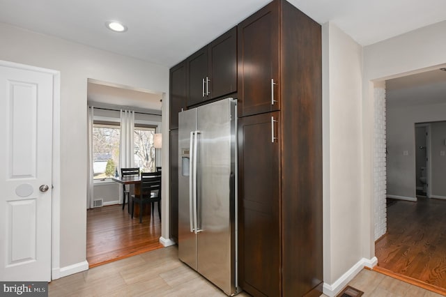 kitchen with dark brown cabinetry, stainless steel fridge, light wood-style flooring, and baseboards