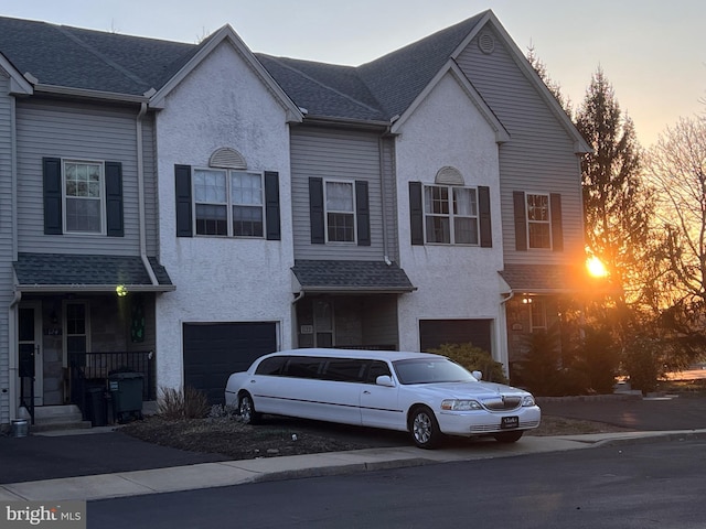 view of property with driveway, a garage, roof with shingles, and stucco siding