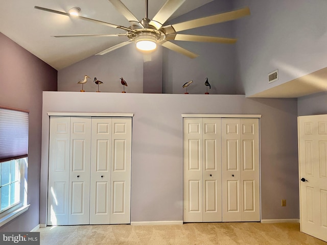 unfurnished bedroom featuring baseboards, visible vents, vaulted ceiling, multiple closets, and light carpet