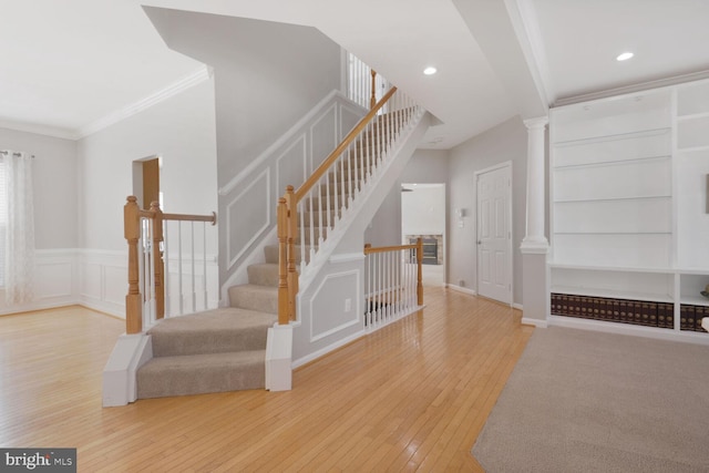 stairs featuring ornamental molding, hardwood / wood-style flooring, built in features, a decorative wall, and decorative columns