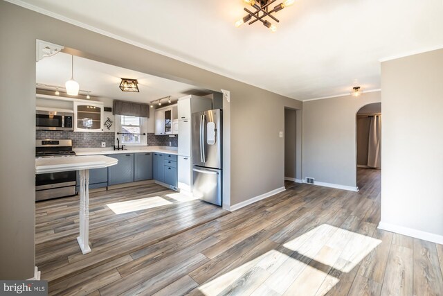 kitchen with arched walkways, decorative backsplash, light countertops, light wood-style floors, and appliances with stainless steel finishes