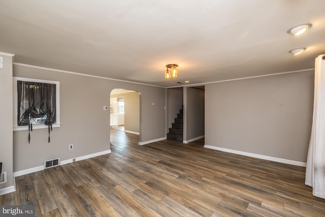 unfurnished living room with visible vents, dark wood finished floors, arched walkways, crown molding, and baseboards