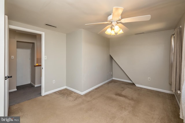 carpeted empty room with visible vents, a ceiling fan, and baseboards