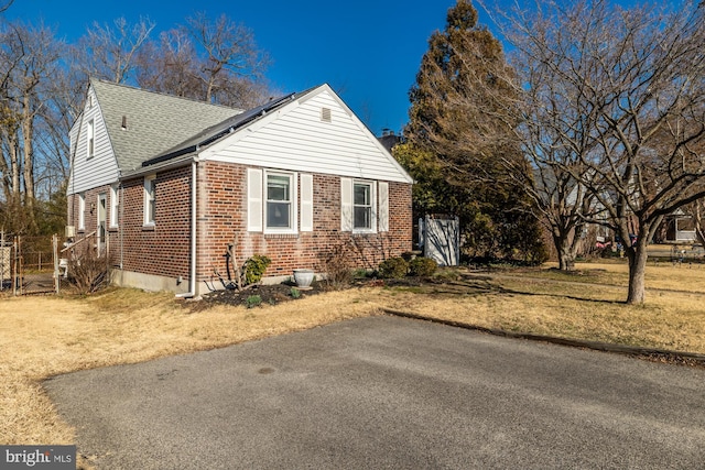 view of side of property featuring a yard, brick siding, and roof with shingles