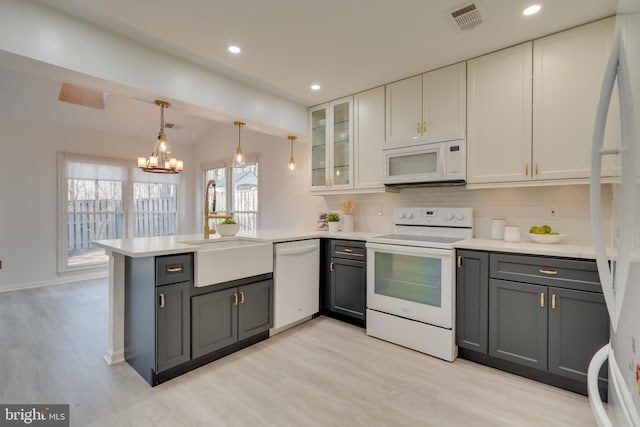 kitchen featuring visible vents, gray cabinetry, a peninsula, white appliances, and a sink