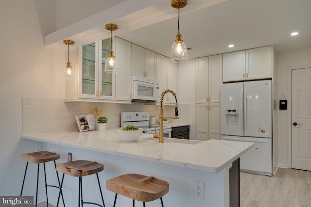 kitchen featuring white appliances, a peninsula, white cabinets, glass insert cabinets, and backsplash