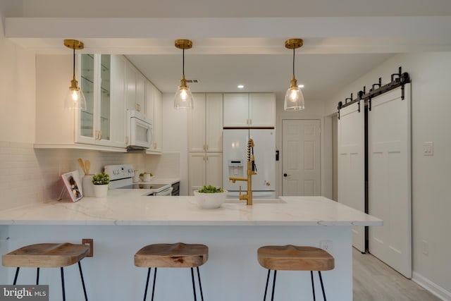 kitchen featuring tasteful backsplash, a barn door, white appliances, a peninsula, and light stone countertops