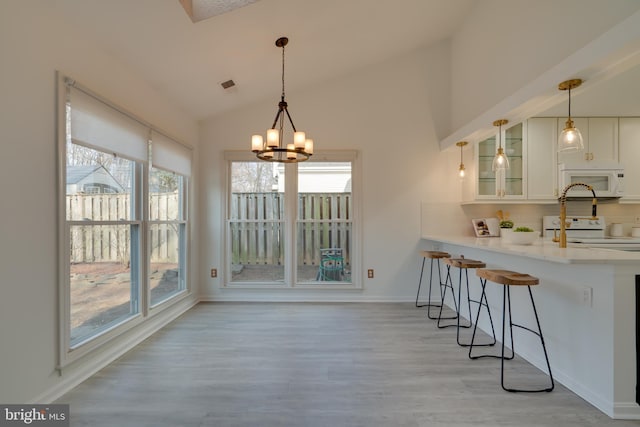 dining room featuring visible vents, baseboards, light wood-type flooring, lofted ceiling, and an inviting chandelier