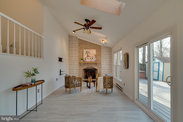 sitting room with a baseboard heating unit, wood finished floors, a skylight, a fireplace, and ceiling fan