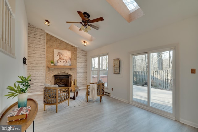 sitting room featuring high vaulted ceiling, light wood-style floors, a skylight, a fireplace, and ceiling fan