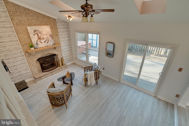 living room featuring wood finished floors, baseboards, ceiling fan, vaulted ceiling, and a brick fireplace