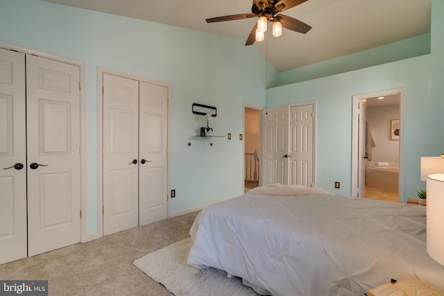 carpeted bedroom with ensuite bath, vaulted ceiling, and two closets