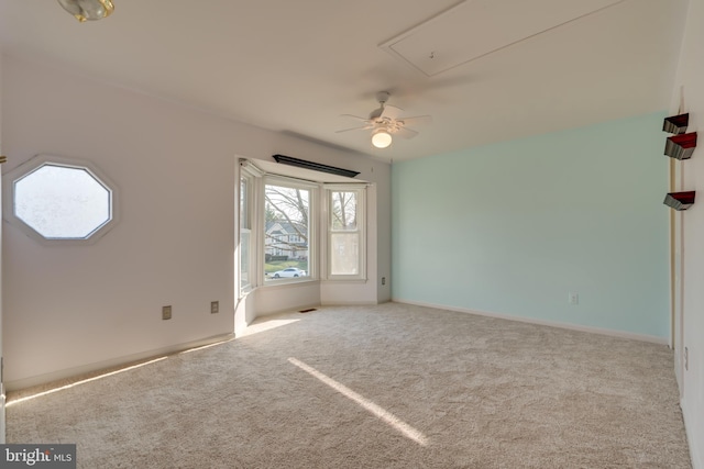 carpeted spare room featuring attic access and ceiling fan