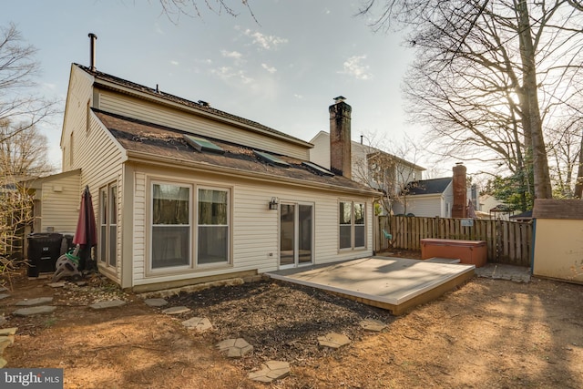 rear view of house featuring a chimney, cooling unit, a hot tub, and fence